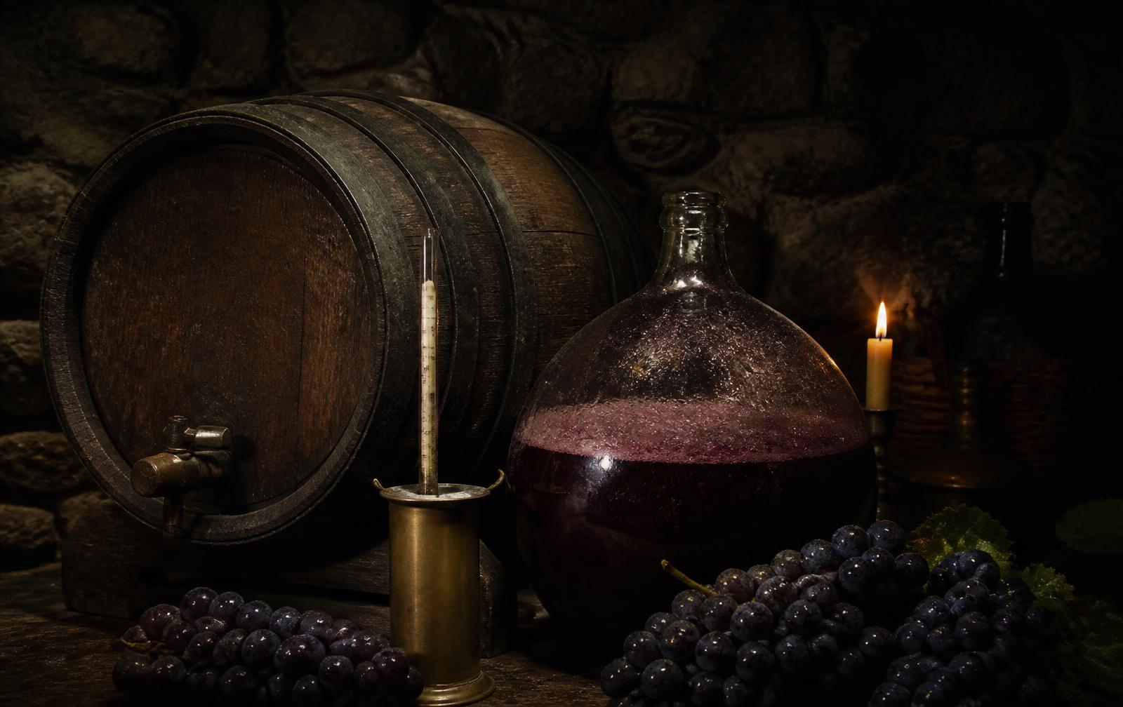 Oak barrel, glass demijohn with wine, and black grapes in a stone cellar
